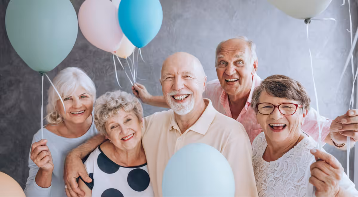 Zu sehen sind 5 fröhliche ältere Menschen jeweils mit einem Luftballon in der in de HAnd.